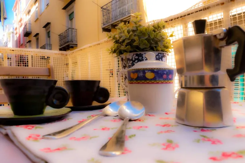 The moka pot and two espresso cups on the floral tablecloth, with the lane behind.