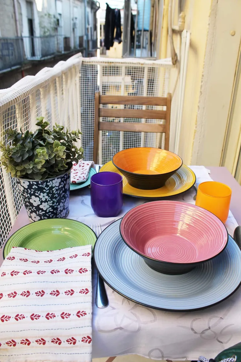 Colourful plates and bowls on the balcony table, with washing hung out across the lane.